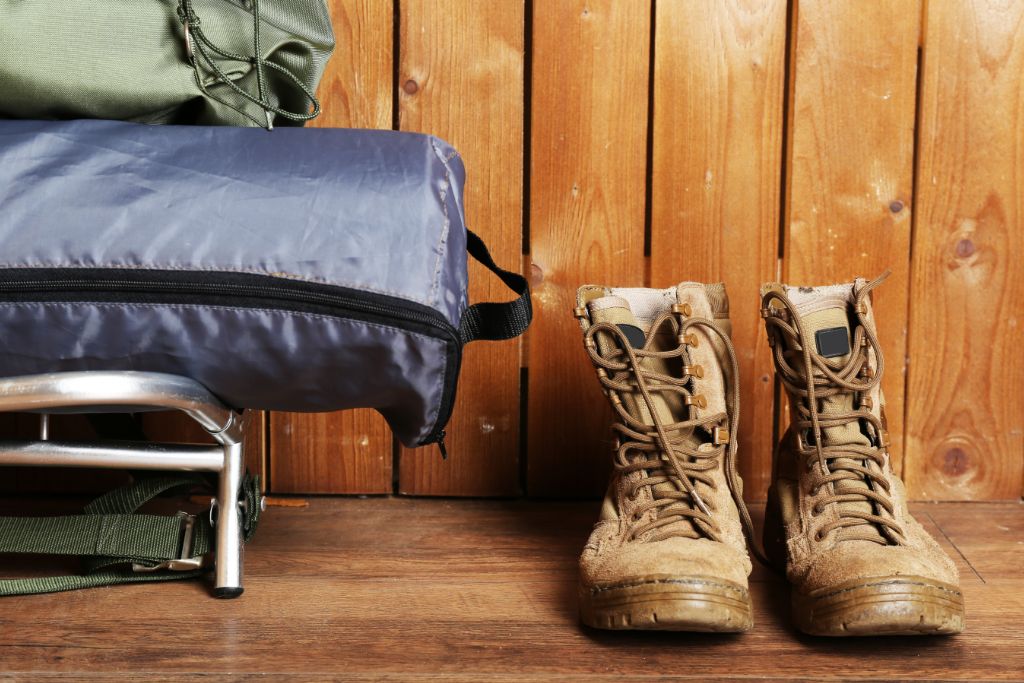 A pair of boots, a sleeping bag, and other essential materials for camping placed on a floor.